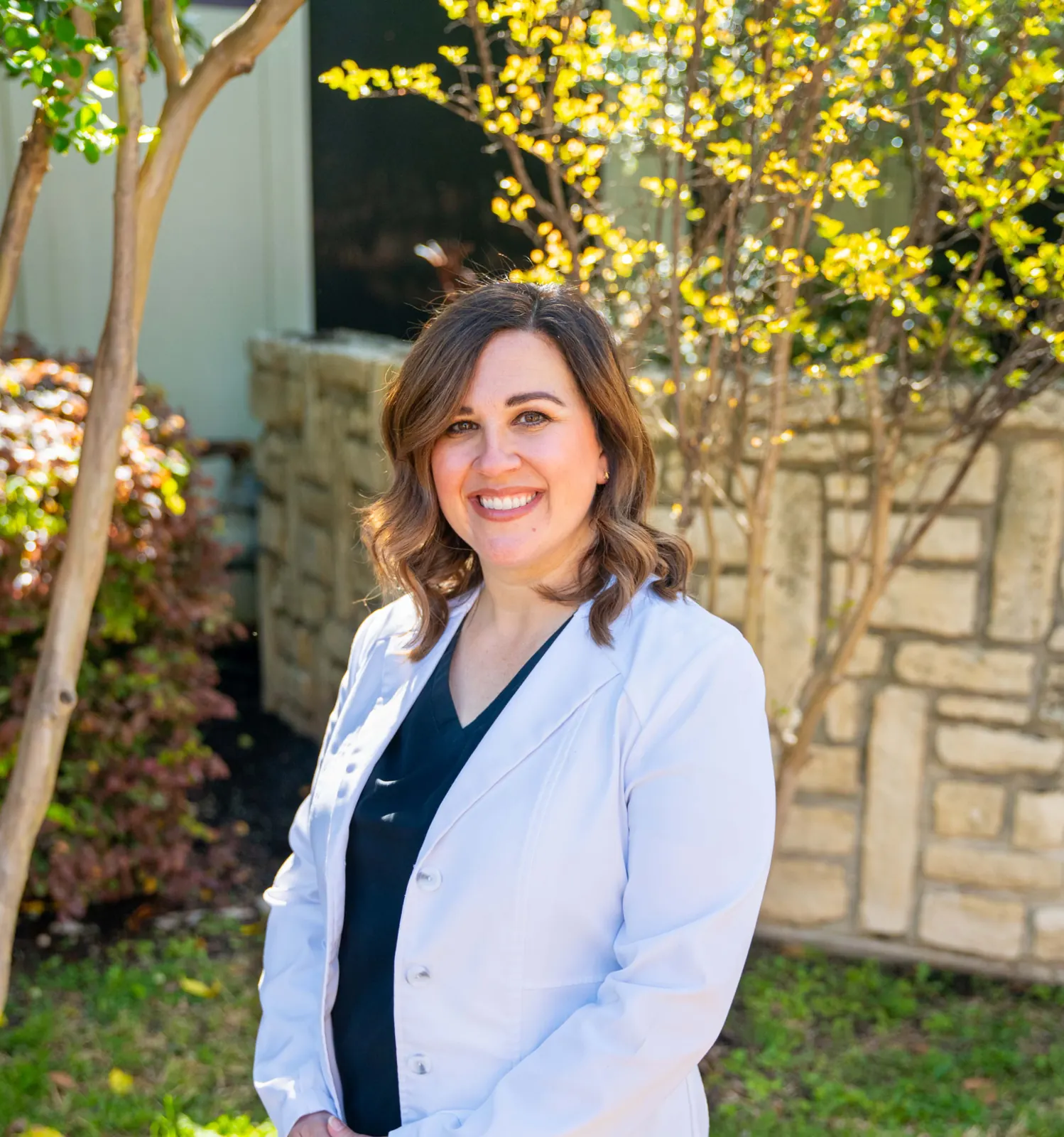Outdoor headshot of a smiling woman in a white coat, by Dark Rainbow Photo Video